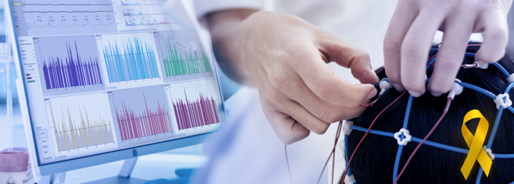 Specjalista zakłada czepek EEG z elektrodami na głowę pacjentki, w tle monitor z analizą widmową sygnału EEG, żółta wstążka Żółtego Września